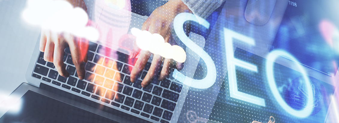 Siglas del SEO Superpuestas sobre Manos Redactando Texto desde Laptop