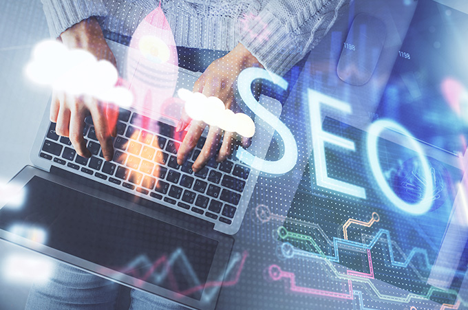 Siglas del SEO Superpuestas sobre Manos Redactando Texto desde Laptop