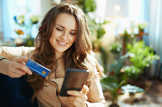 Chica Sentada Sosteniendo su Tarjeta de Crdito Mientras Compra en su Telfono
