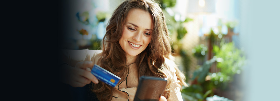 Chica Sentada Sosteniendo su Tarjeta de Crdito Mientras Compra en su Telfono