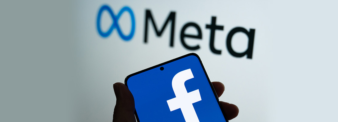 Mano Sosteniendo Smartphone con el Logo de Facebook y Logo de Metaverso Detrás