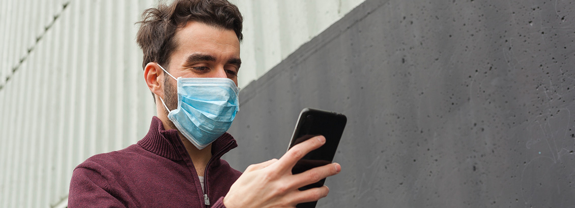 Hombre con Tapabocas en Exteriores Revisando Facebook Desde su Smartphone