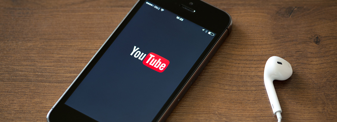 Smartphone Mostrando YouTube en su Pantalla y Audífono a un Lado