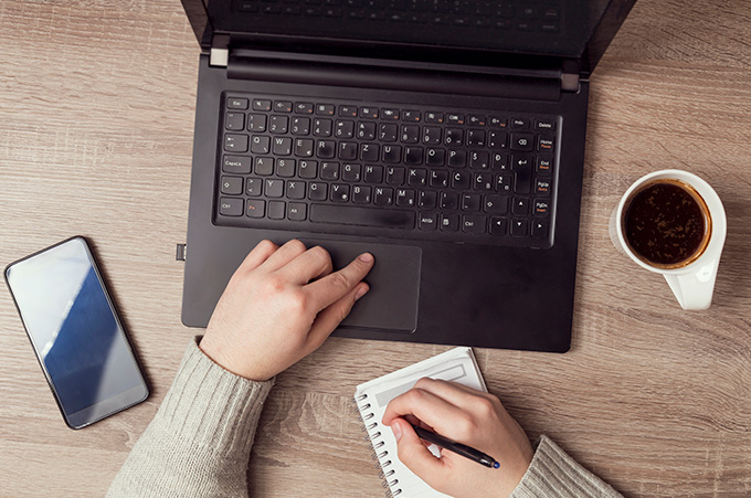 Community Manager Sentado en Escritorio Mientras Planifica en su Bloc de Notas Frente a Laptop