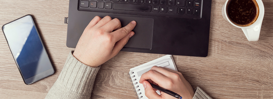 Community Manager Sentado en Escritorio Mientras Planifica en su Bloc de Notas Frente a Laptop