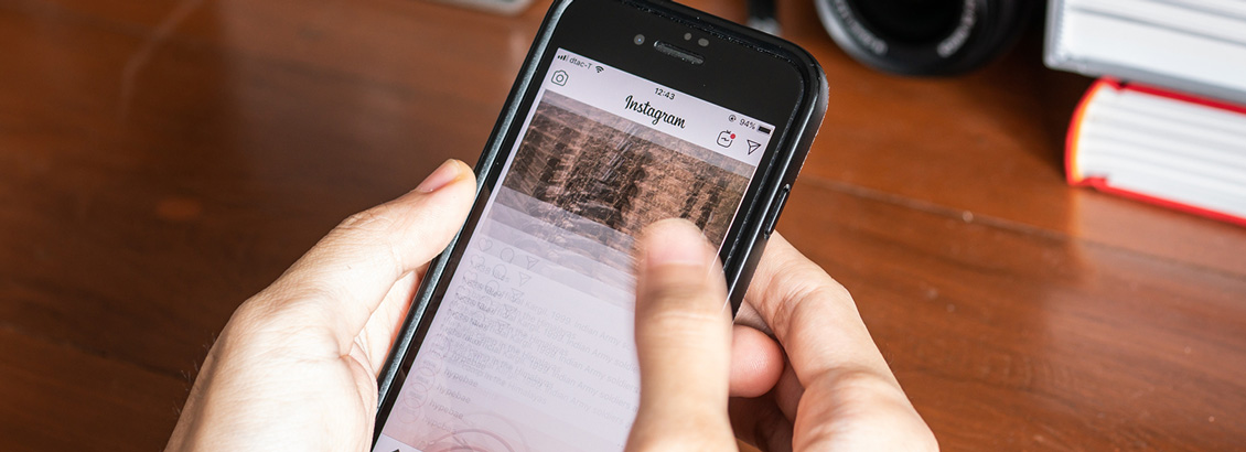 Manos Sosteniendo Smartphone y Trazando Feed de Instagram en la Pantalla