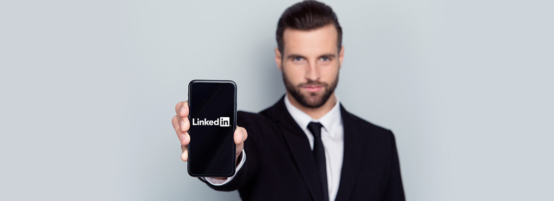 Empresario Mostrando Smartphone a la Cámara con Logo de LinkedIn en Pantalla