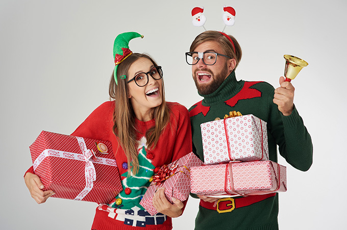 Pareja Geek Vestida con Sweaters Navideos y Sosteniendo Regalos