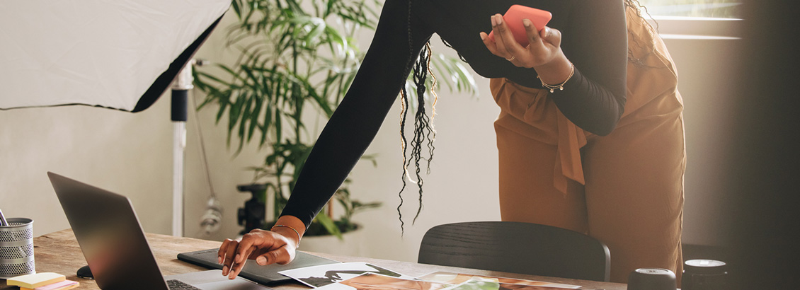 Mujer de Negocios Sosteniendo Celular y Actualizando su Perfil de Instagram desde una Laptop