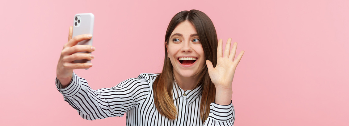 Mujer Joven Sonriente que Saluda con una Mano Frente a su Smartphone